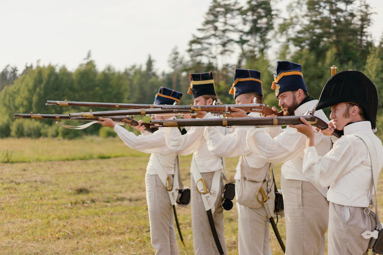 Soldiers in vintage uniforms aiming rifles during a historical battle reenactment outdoors.